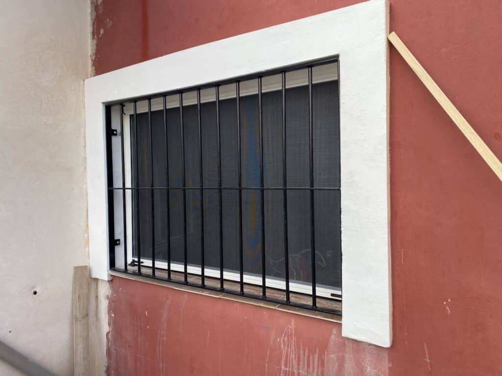 Reja metálica negra con barrotes verticales y placas laterales de fijación