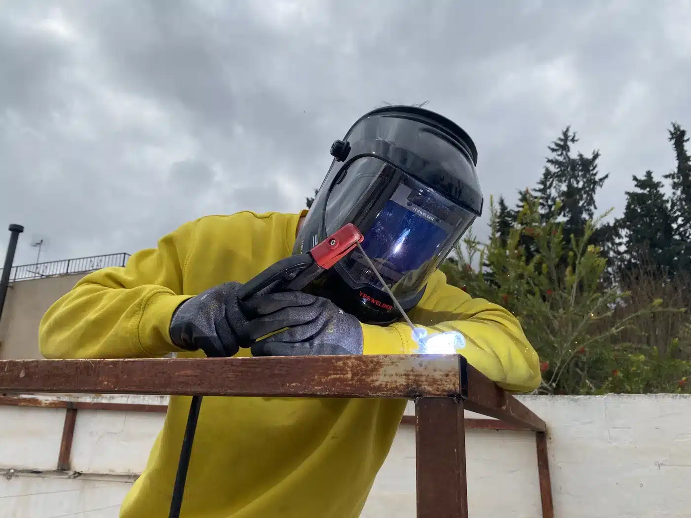 Profesional con pantalla de protección soldando un elemento de hierro