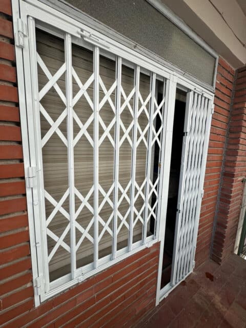 Reja blanca delante de una ventana y cierre de ballesta recogido junto a la puerta